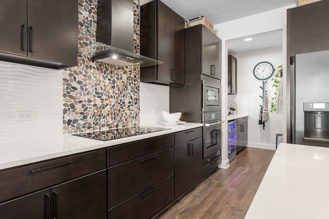 kitchen featuring dark wood-style flooring, stainless steel appliances, light countertops, decorative backsplash, and wall chimney exhaust hood