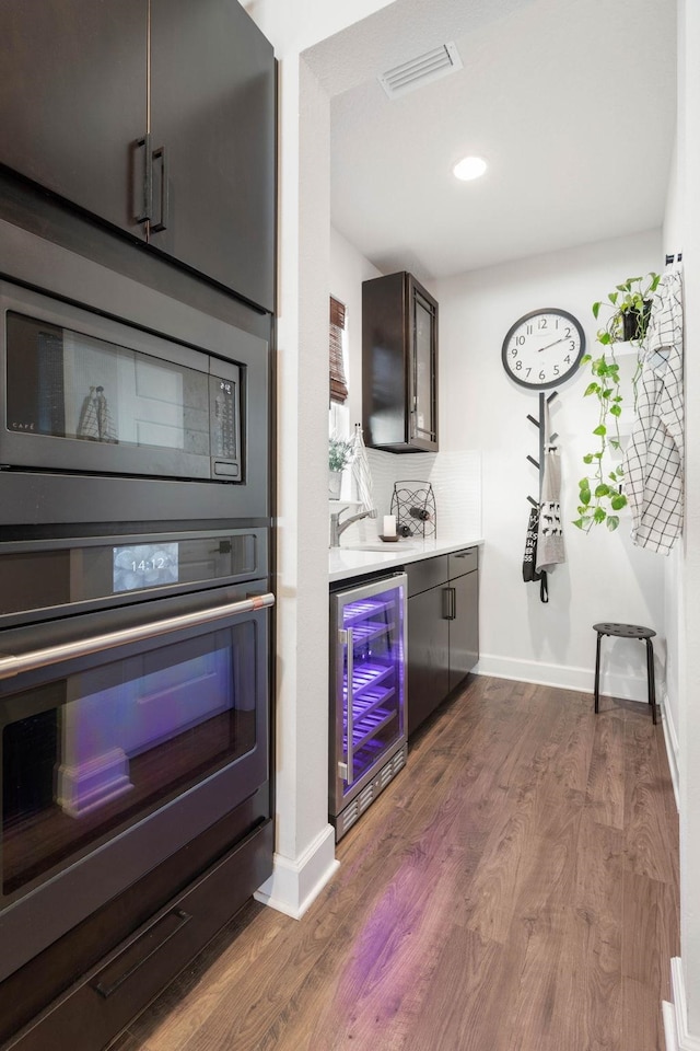 bar featuring visible vents, dark wood-type flooring, built in microwave, beverage cooler, and oven