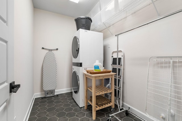 washroom with baseboards, laundry area, dark tile patterned flooring, and stacked washer / drying machine