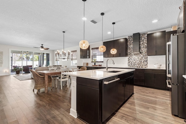 kitchen featuring visible vents, appliances with stainless steel finishes, open floor plan, wall chimney range hood, and a sink