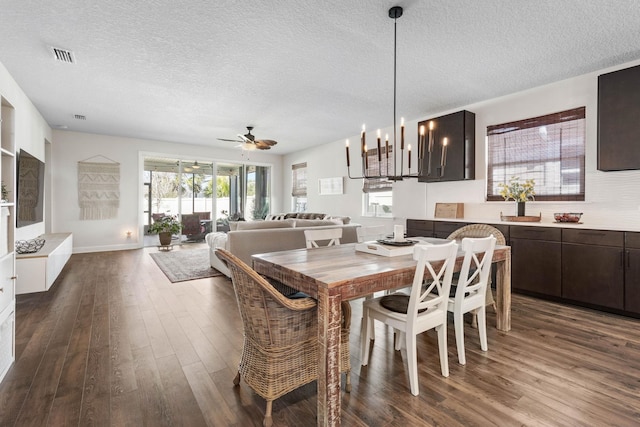 dining room featuring dark wood-type flooring, visible vents, a textured ceiling, and ceiling fan with notable chandelier