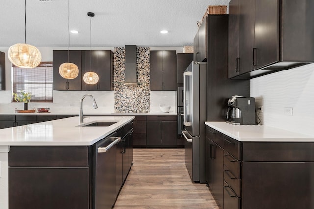 kitchen with stainless steel appliances, a sink, light countertops, wall chimney range hood, and dark brown cabinets