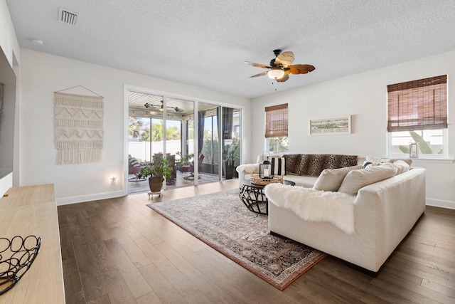 living room featuring baseboards, visible vents, a ceiling fan, dark wood-style flooring, and a textured ceiling