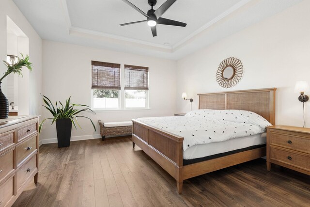 bedroom featuring baseboards, ceiling fan, dark wood-style flooring, a tray ceiling, and crown molding