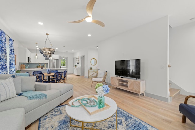 living room with ceiling fan with notable chandelier and light hardwood / wood-style flooring