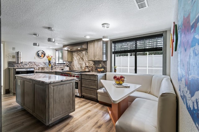 kitchen featuring a center island, stainless steel stove, pendant lighting, and wall chimney range hood