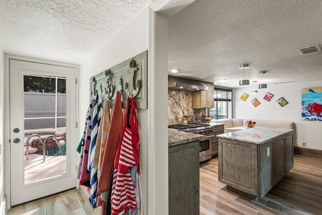 kitchen with wall chimney exhaust hood, light hardwood / wood-style flooring, high end stove, a textured ceiling, and a kitchen island