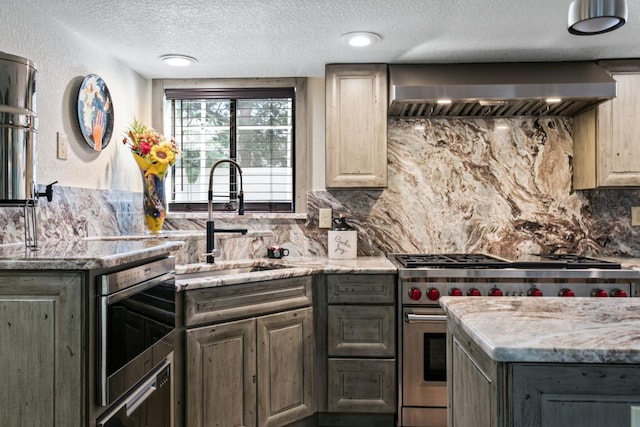 kitchen with range with two ovens, wall chimney range hood, sink, decorative backsplash, and a textured ceiling