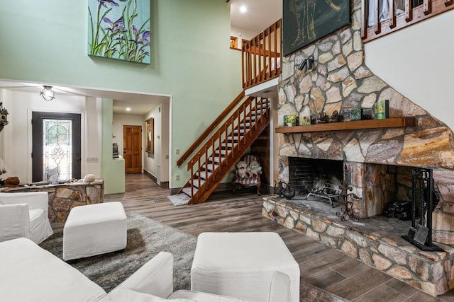 living room featuring wood-type flooring, a stone fireplace, and a high ceiling