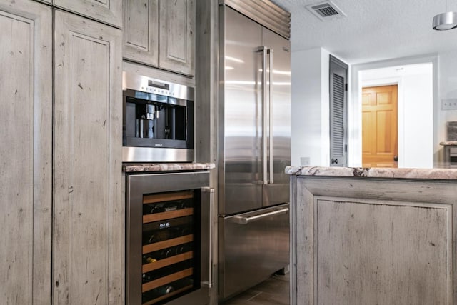 kitchen featuring a textured ceiling, wine cooler, light stone counters, and stainless steel built in refrigerator