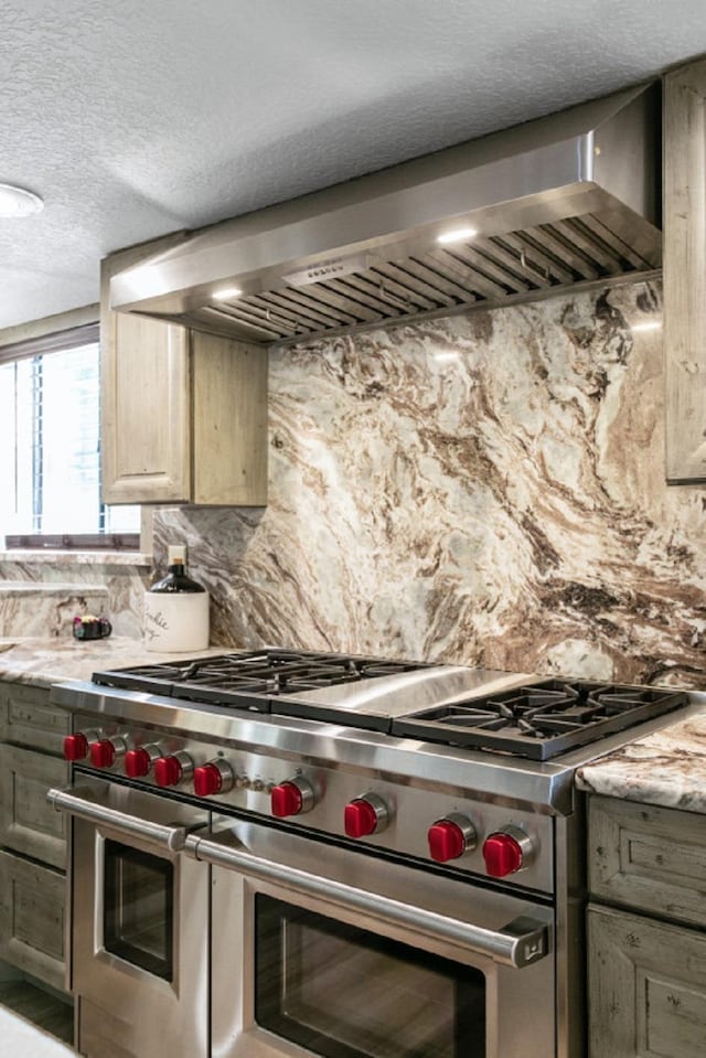 kitchen featuring light stone countertops, backsplash, double oven range, and wall chimney exhaust hood