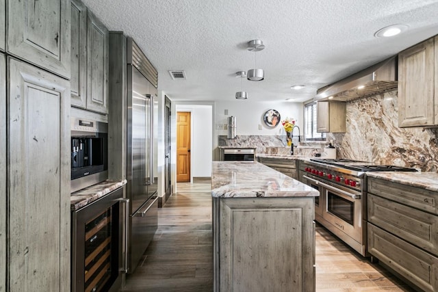 kitchen with a center island, beverage cooler, wall chimney range hood, premium appliances, and wood-type flooring