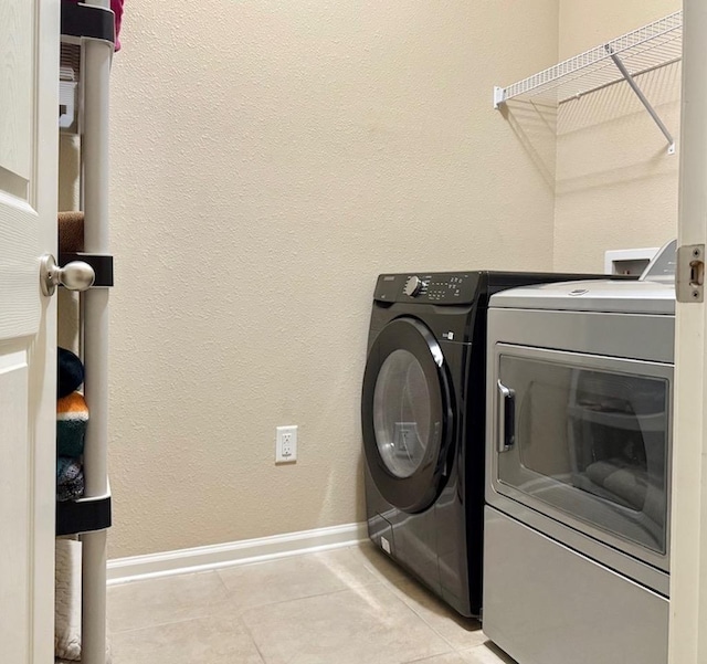 clothes washing area featuring separate washer and dryer, baseboards, and light tile patterned flooring