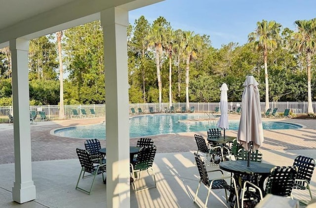 community pool featuring fence, a patio, and view of scattered trees