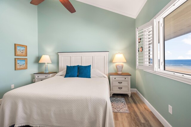 bedroom with crown molding, a water view, vaulted ceiling, light wood-type flooring, and baseboards