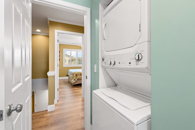 laundry area with laundry area, a ceiling fan, baseboards, light wood-style floors, and stacked washer and clothes dryer