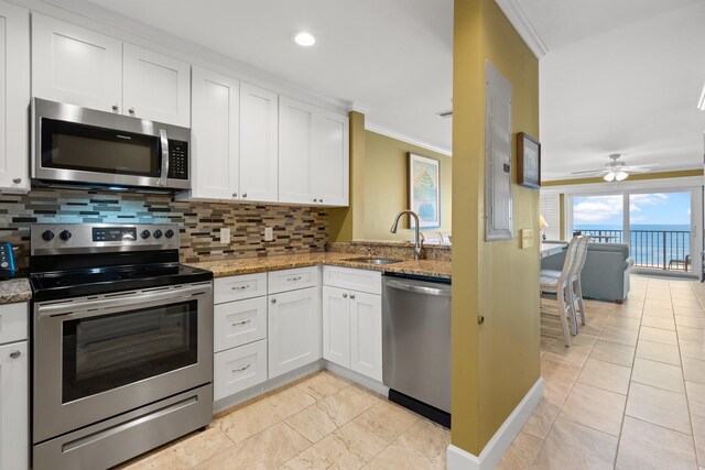 kitchen with crown molding, appliances with stainless steel finishes, stone countertops, white cabinets, and a sink