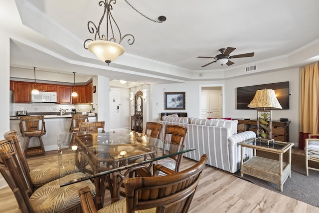 dining space with ceiling fan, ornamental molding, a raised ceiling, and light hardwood / wood-style floors