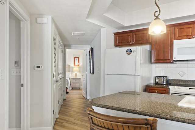 kitchen with white appliances, backsplash, decorative light fixtures, dark stone counters, and light wood-type flooring