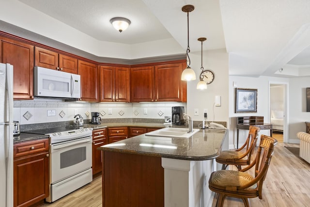 kitchen featuring sink, kitchen peninsula, pendant lighting, white appliances, and backsplash