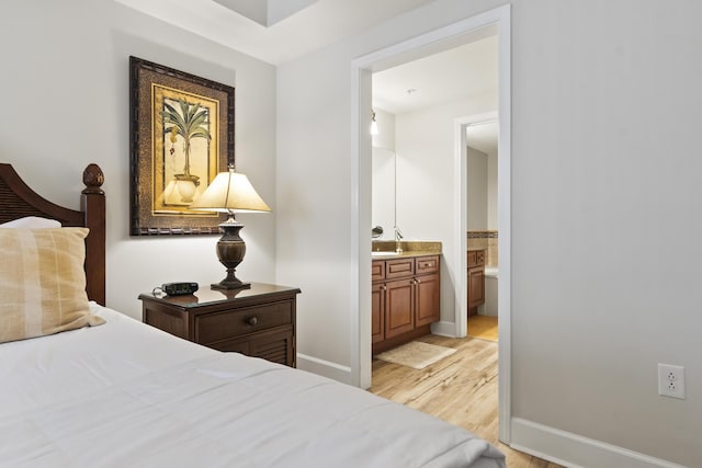 bedroom with sink, ensuite bath, and light wood-type flooring