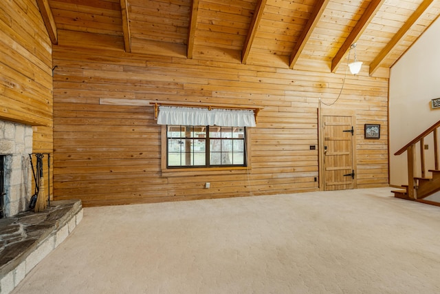 unfurnished living room featuring wood walls, a stone fireplace, carpet flooring, beam ceiling, and wood ceiling