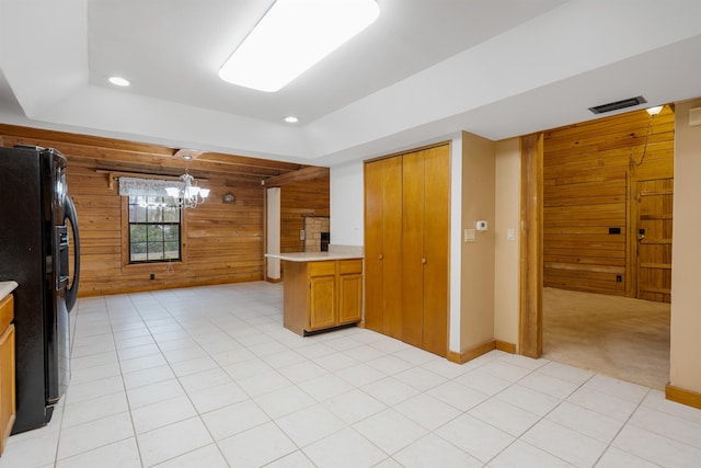 kitchen with light carpet, black fridge, kitchen peninsula, decorative light fixtures, and wooden walls