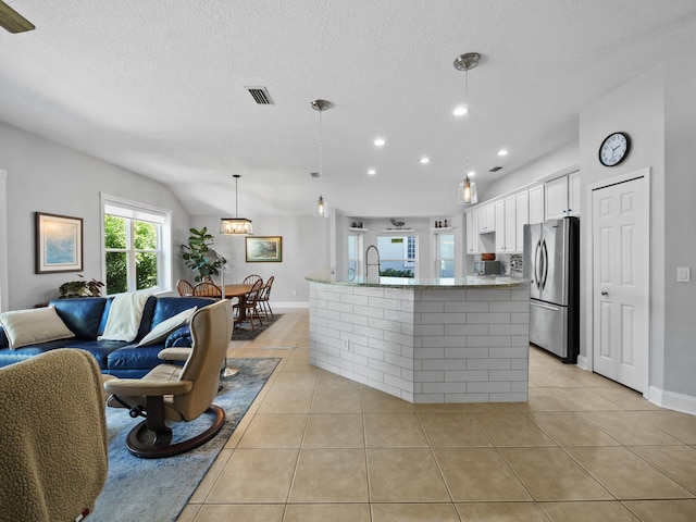 kitchen with light tile patterned flooring, a center island with sink, hanging light fixtures, stainless steel refrigerator, and white cabinets