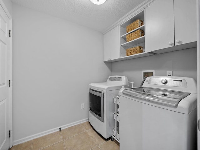 clothes washing area featuring cabinets, washer and dryer, light tile patterned floors, and a textured ceiling