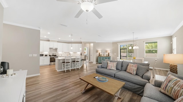 living room featuring ceiling fan with notable chandelier, light wood-type flooring, and ornamental molding