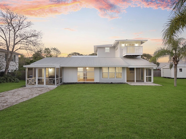 back house at dusk featuring a yard, a balcony, and a sunroom