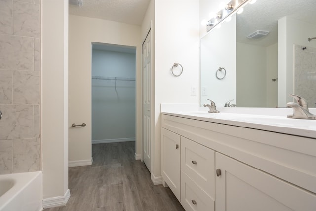 bathroom featuring vanity, wood-type flooring, a textured ceiling, and tiled shower / bath combo