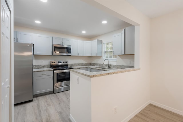 kitchen with kitchen peninsula, light stone counters, stainless steel appliances, sink, and light hardwood / wood-style floors