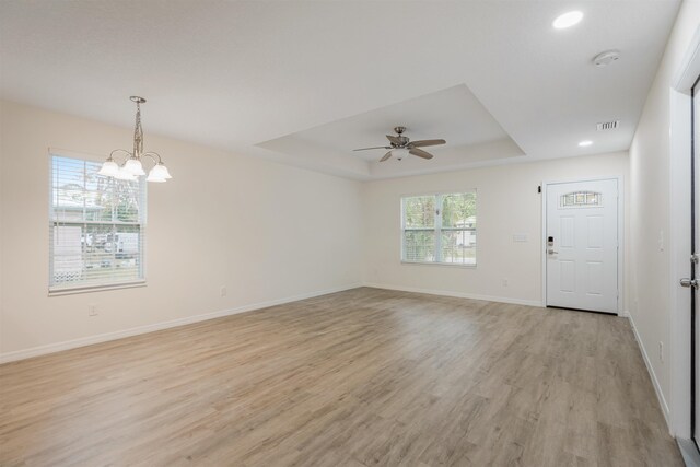 interior space with ceiling fan with notable chandelier, light hardwood / wood-style floors, and a raised ceiling