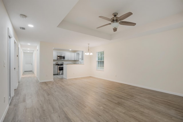 unfurnished living room featuring a tray ceiling, light hardwood / wood-style flooring, ceiling fan with notable chandelier, and sink