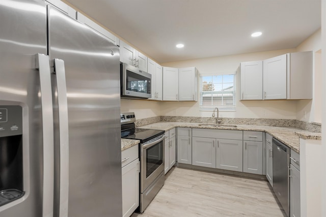 kitchen featuring light stone countertops, sink, light wood-type flooring, and appliances with stainless steel finishes