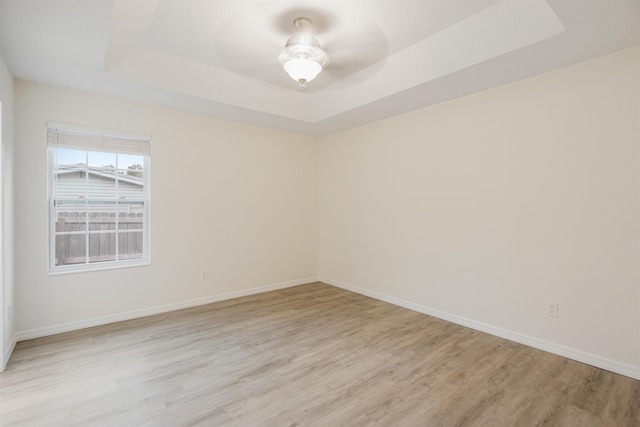 unfurnished room with a raised ceiling, ceiling fan, and light wood-type flooring