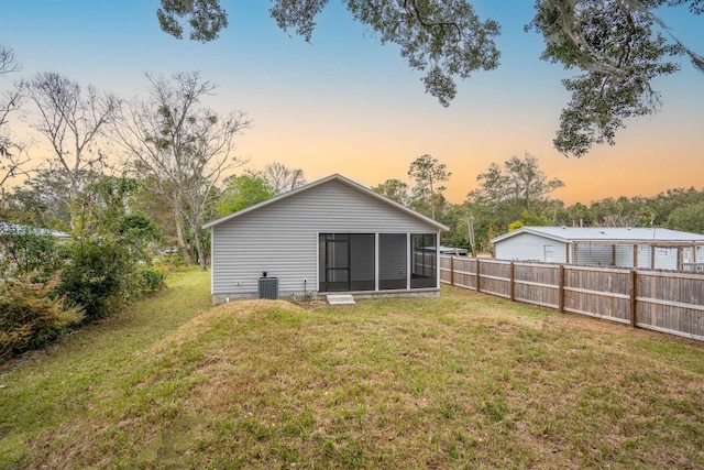 back house at dusk featuring a sunroom, cooling unit, and a yard