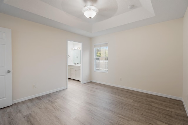 unfurnished bedroom featuring a raised ceiling, ceiling fan, sink, hardwood / wood-style floors, and connected bathroom