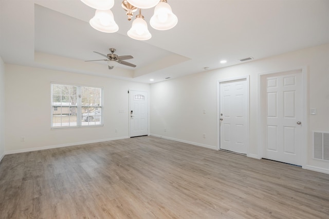 spare room featuring a raised ceiling, ceiling fan with notable chandelier, and light hardwood / wood-style flooring