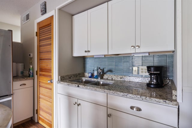 kitchen featuring light stone counters, white cabinetry, sink, and stainless steel refrigerator