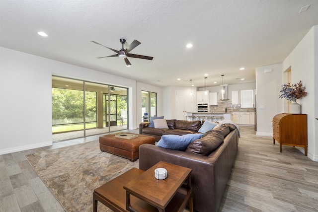 living room with ceiling fan, a textured ceiling, and light wood-type flooring