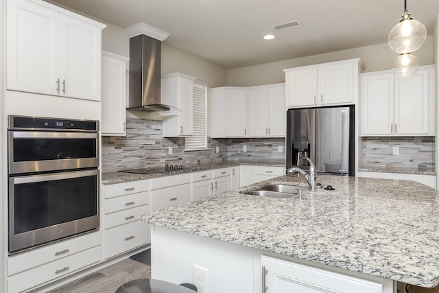 kitchen with white cabinetry, sink, stainless steel appliances, wall chimney range hood, and an island with sink