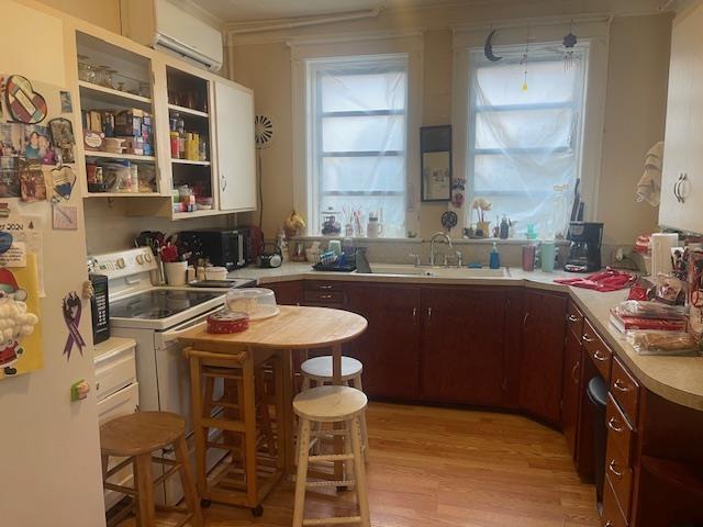 kitchen with dark brown cabinets, sink, an AC wall unit, white electric range, and light hardwood / wood-style floors