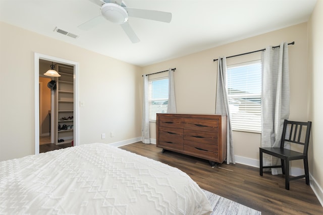 bedroom featuring baseboards, visible vents, dark wood-style flooring, ceiling fan, and a walk in closet