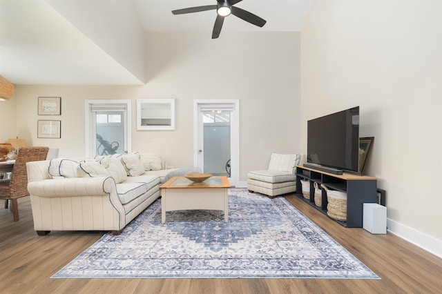 living room featuring baseboards, wood finished floors, ceiling fan, and a towering ceiling