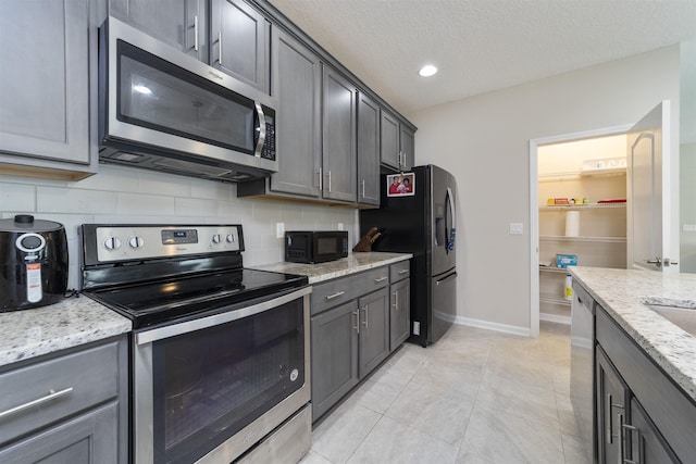 kitchen with backsplash, light stone counters, a textured ceiling, stainless steel appliances, and light tile patterned flooring