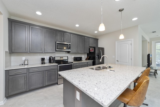 kitchen featuring black appliances, pendant lighting, light stone counters, and an island with sink