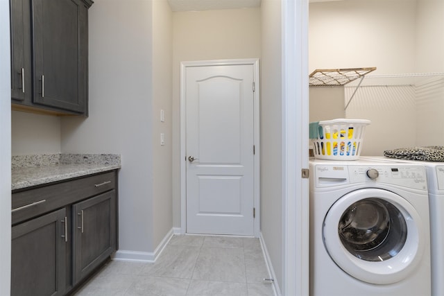 clothes washing area featuring washing machine and clothes dryer, light tile patterned floors, and cabinets