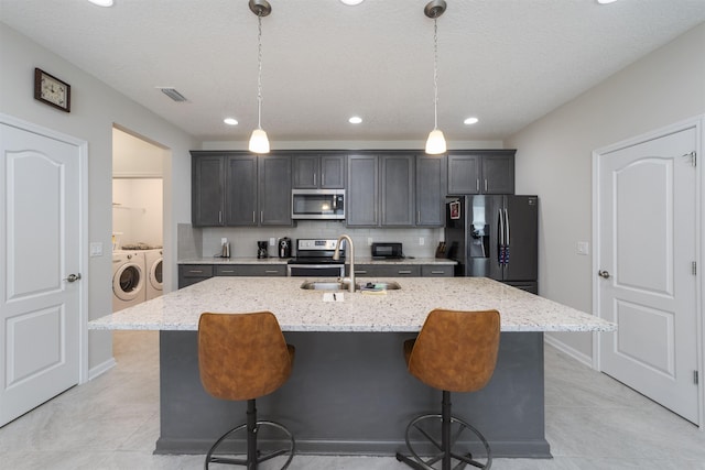 kitchen with a center island with sink, hanging light fixtures, appliances with stainless steel finishes, and washing machine and clothes dryer